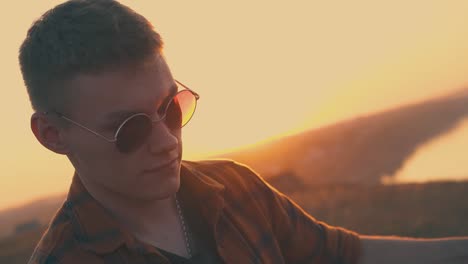 tipo feliz con gafas de sol toca la guitarra en el campamento turístico