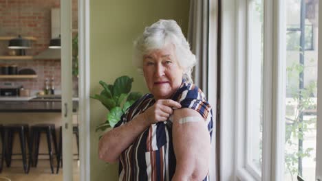 happy caucasian senior woman showing plaster on arm after covid vaccination