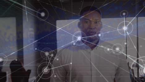 Animation of biracial businessman standing in office, dots connected with lines and abstract pattern