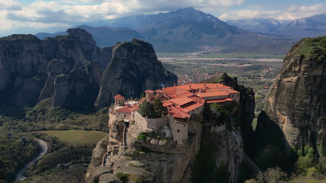 Cinematic aerial establishing monastery on cliff edge in Kalambaka, Greece under sunny skies