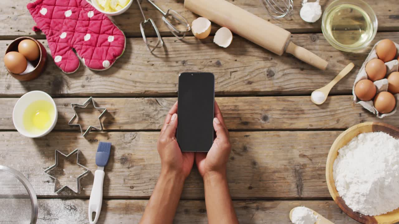video de manos de una mujer sosteniendo un teléfono inteligente con espacio de copia sobre ingredientes y herramientas de horneado