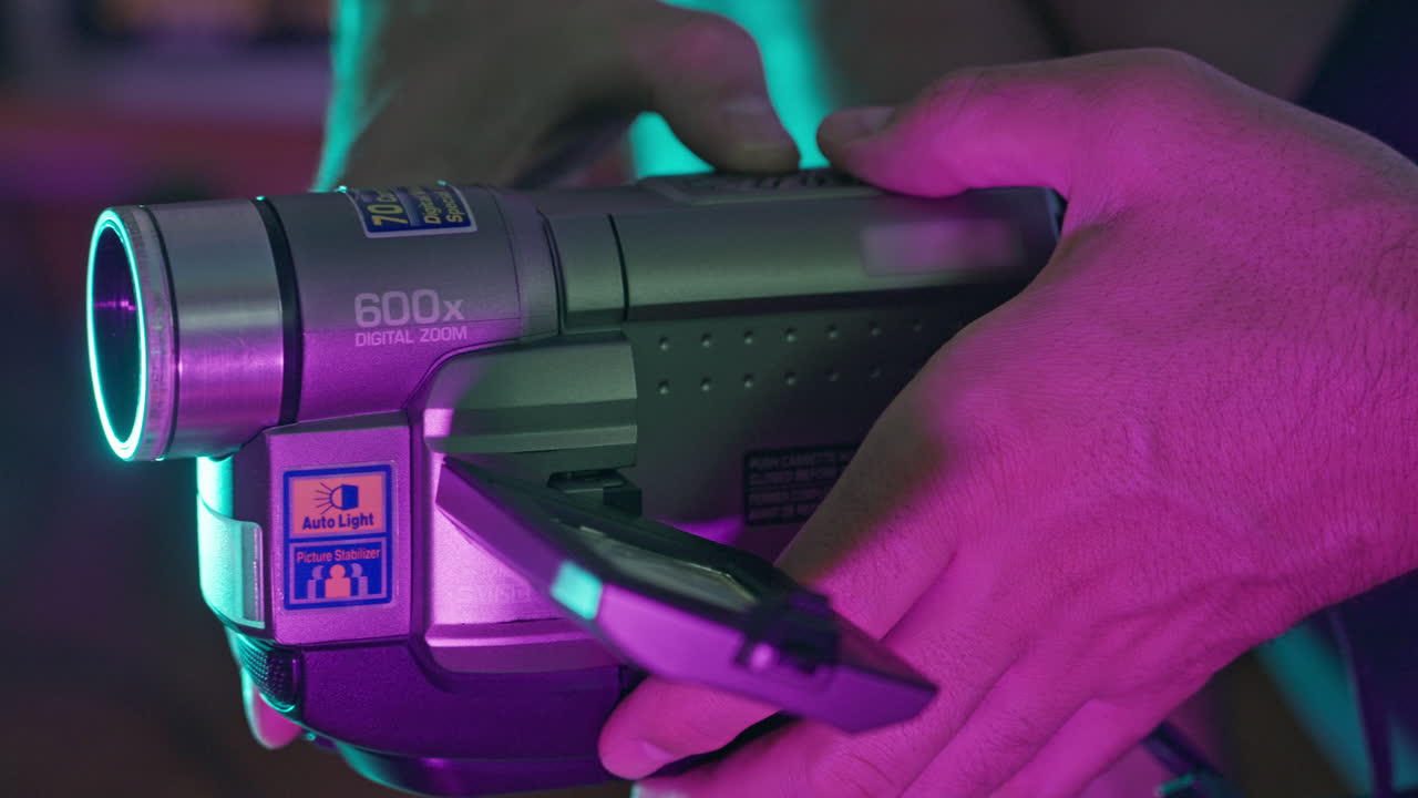 Close-Up of Hands Holding a Retro Digital Camcorder with Neon Lights