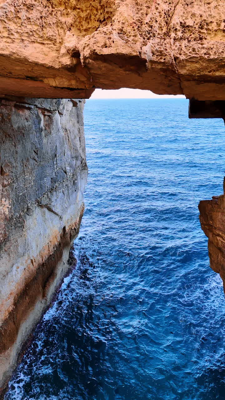 People sit on the bare rock at the shore of the Mediterranean Sea. Coast of Malta, Europe. Vertical video.