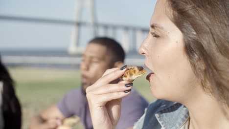 un primer plano de una mujer joven y tranquila comiendo pizza en el parque.