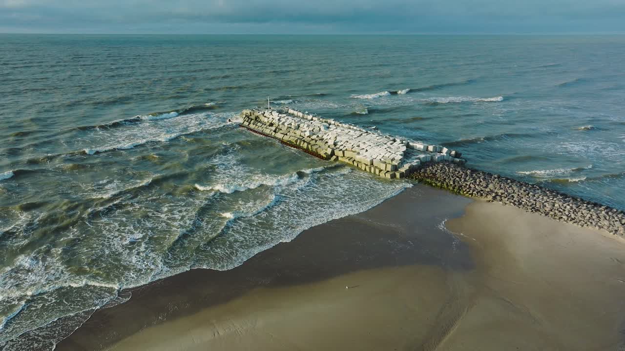 Aerial establishing view of protective stone pier with concrete blocks and rocks at Baltic sea coastline at Liepaja, Latvia, strengthening beach against coastal erosion, wide drone shot moving forward