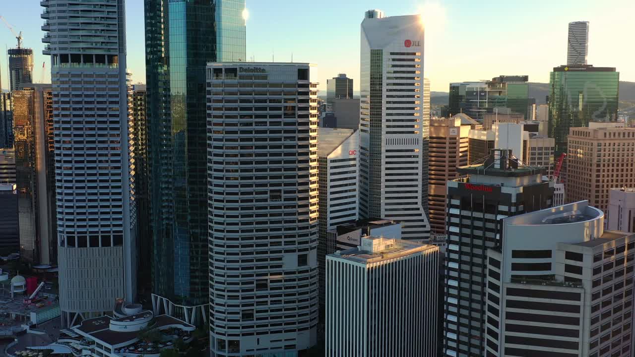 Aerial flyover the Brisbane river capturing riverside downtown cityscape of Brisbane city, with towering skyscrapers bathed in golden sunset light.