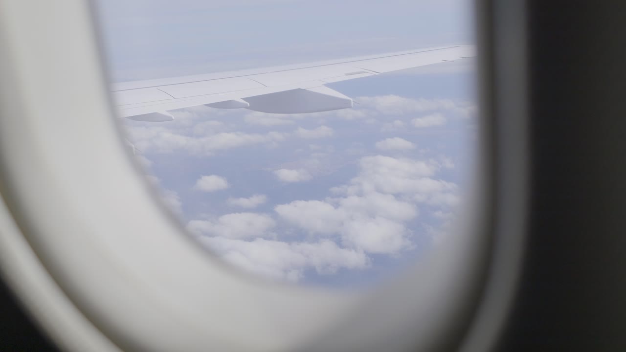 View from airplane window showing wing over fluffy clouds on a clear day