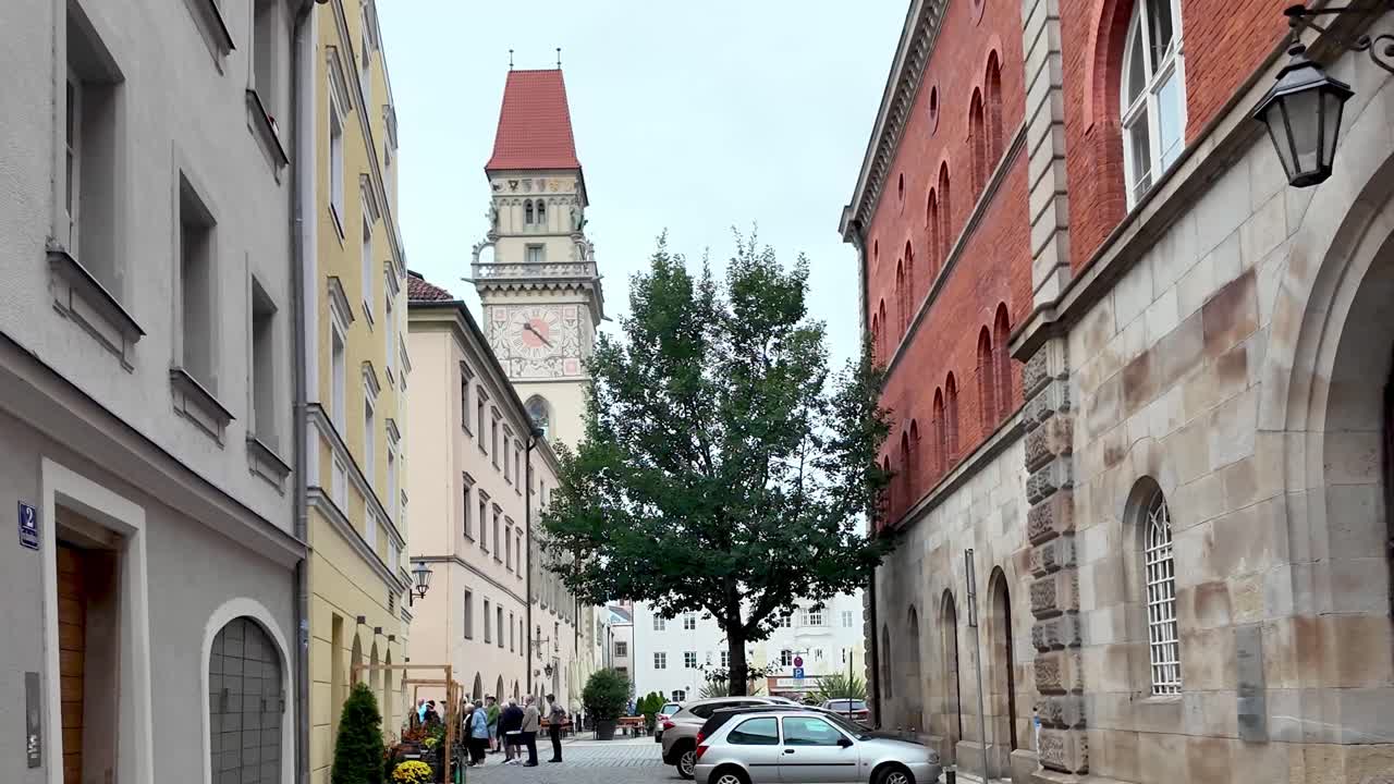 Town hall tower in the distant with cobbled street, people, and parked cars in Passau, Bavaria, Germany
