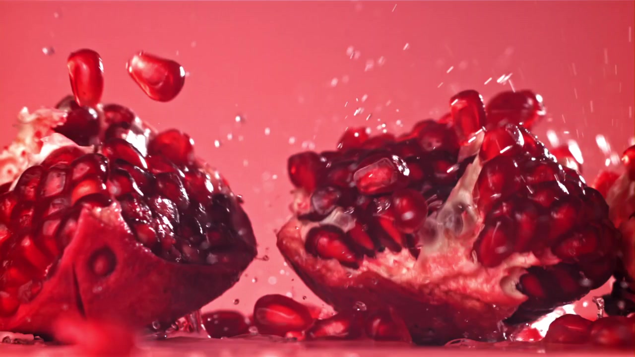 Slowmotion granatæblehalvdele der sprøjter med vanddråber