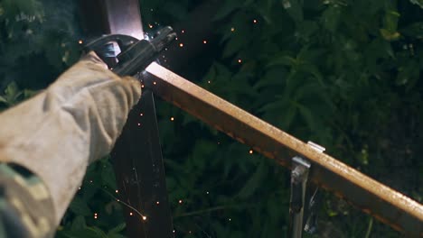 closeup-builder-welds-parts-of-fence-against-green-plants