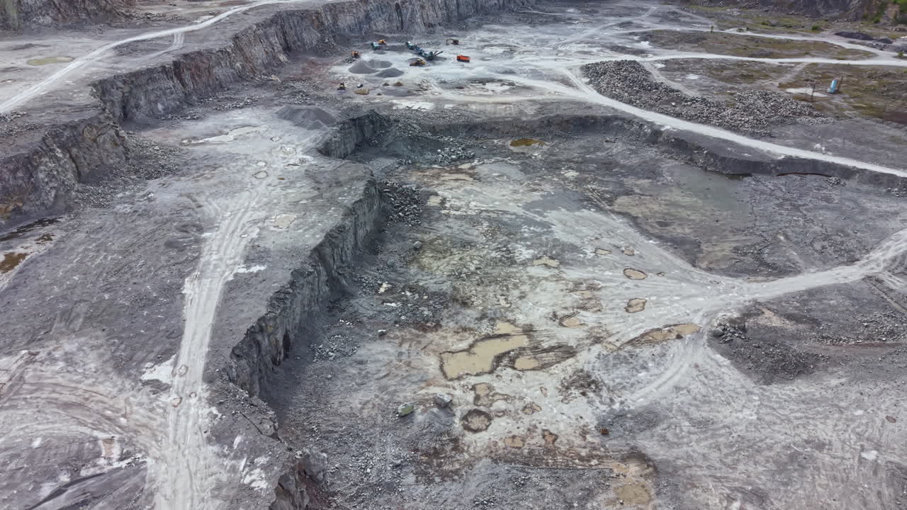 Mining site shows large quarry with vehicles and heavy machinery in operation during daylight hours