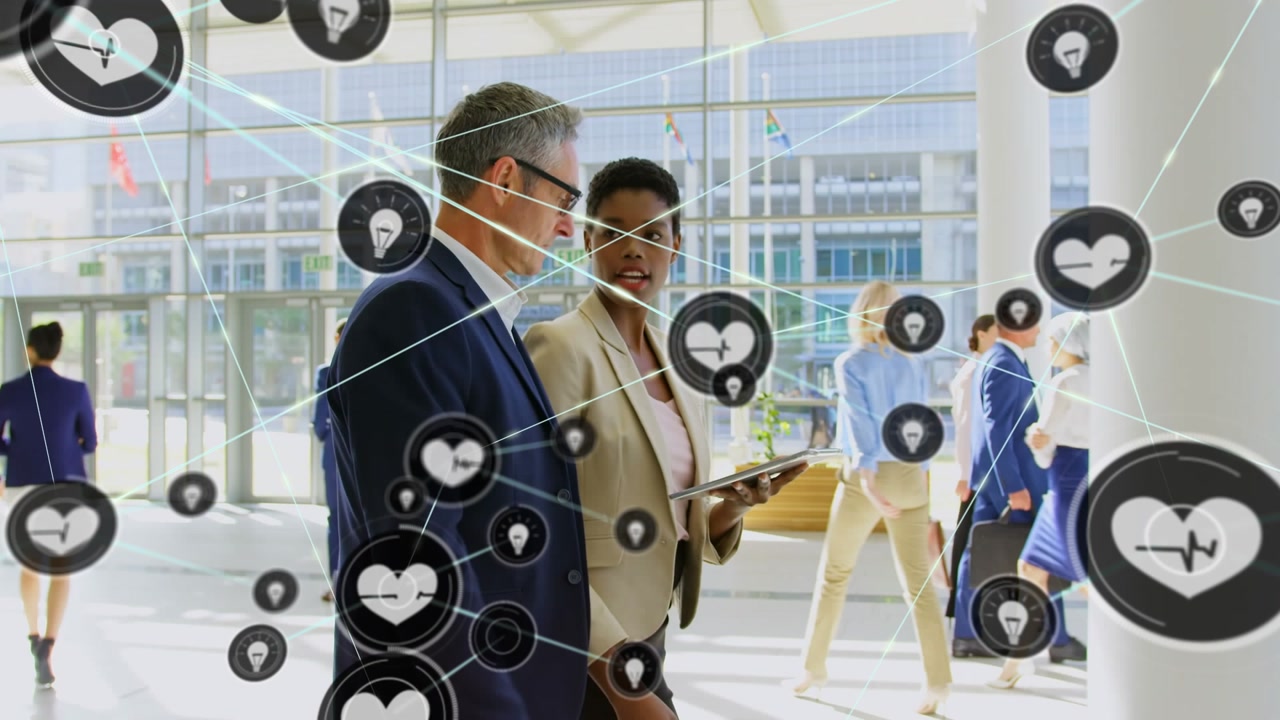 Heart and lightbulb icons connecting with lines over multiracial coworkers discussing in corridor