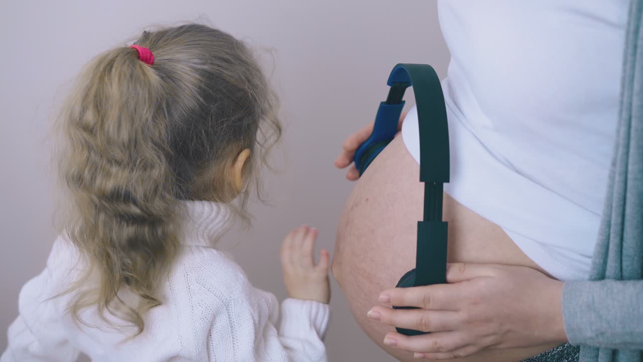 임신 한 엄마 와 함께 재 ⁇ 는 소녀 는 배 에 헤드폰 을 착용 한다