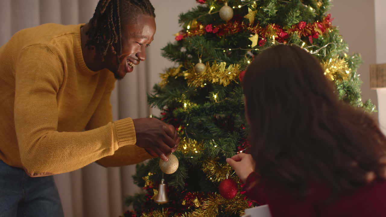 una pareja feliz decorando el árbol de navidad en casa, en cámara lenta.