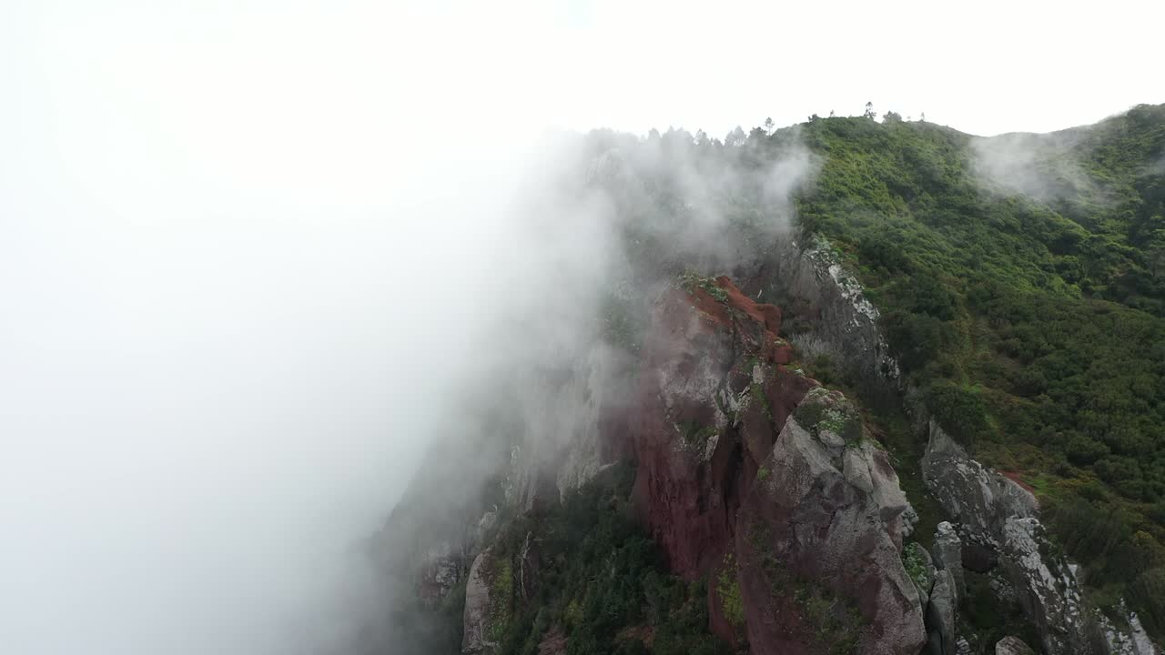 드론 샷이 위아래로 움직이며 두꺼운 구름이 움직이고 정상을 둘러싸고 있는 마데이라의 에스피가오 아모렐로 절벽을 드러냅니다.
