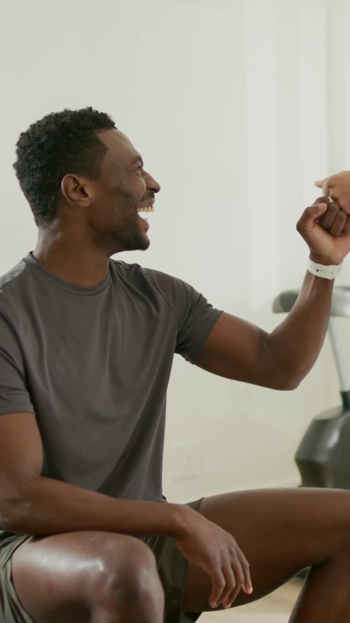 Vertical video: Leaning, man in gray shirt checking white watch in home gym, trainer helping