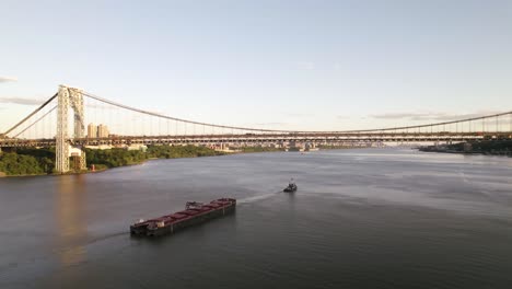 industrial barge traveling up hudson river toward new york city skyline at golden hour
