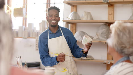 happy african american potter working with others in pottery studio, slow motion