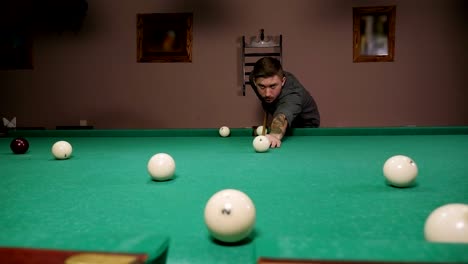 a brutal man with tattoos on his hands is playing russian billiards in a bar.