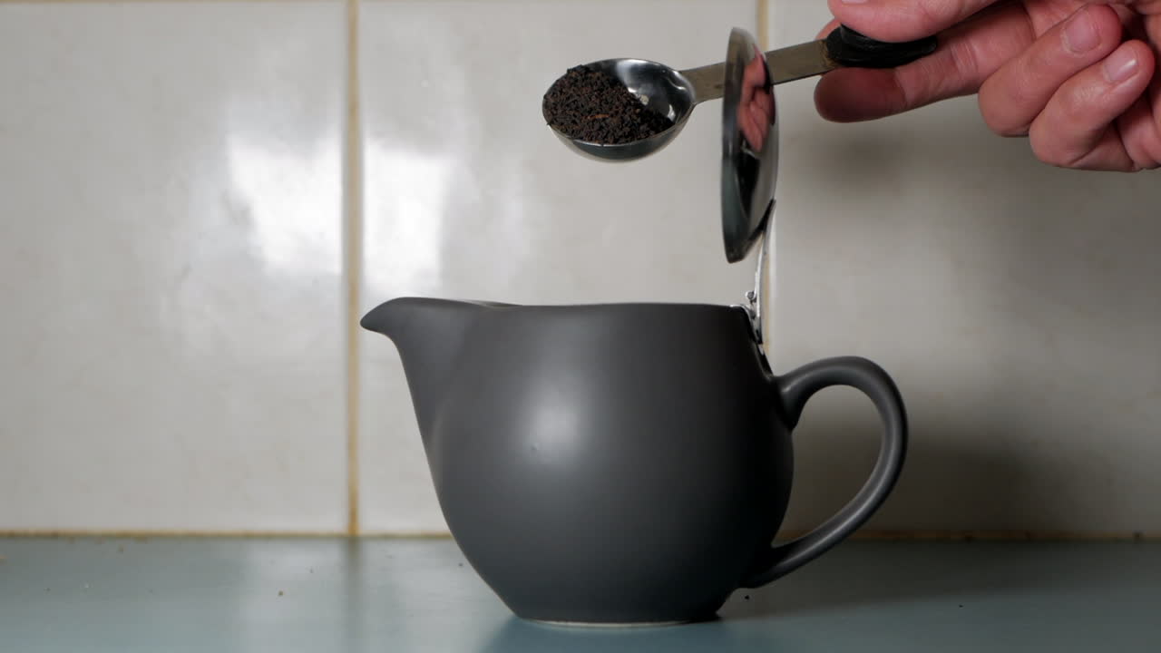 hojas de té vertidas o volcadas en una olla moderna en la cocina de un hogar