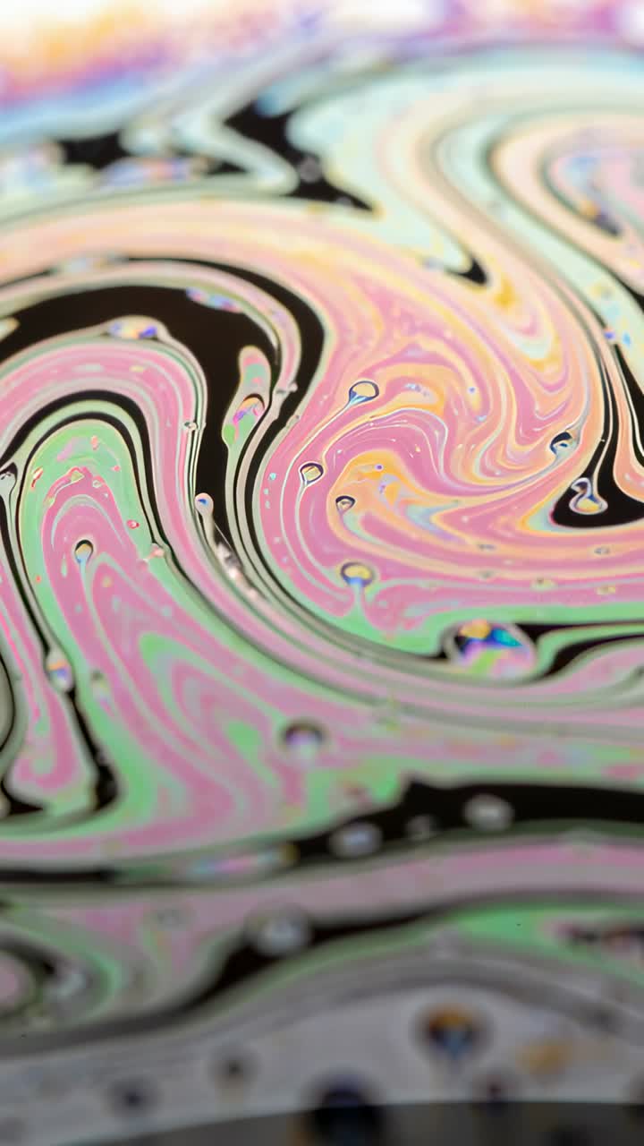 Video verticale: Pellicola di sapone cangiante che mostra linee e perline nere mentre la messa a fuoco si sposta in macro studio.