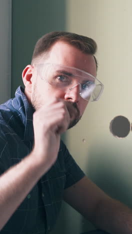 CU: builder with transparent goggles proud of finished work shows just switched lever on light green wall at renewal closeup