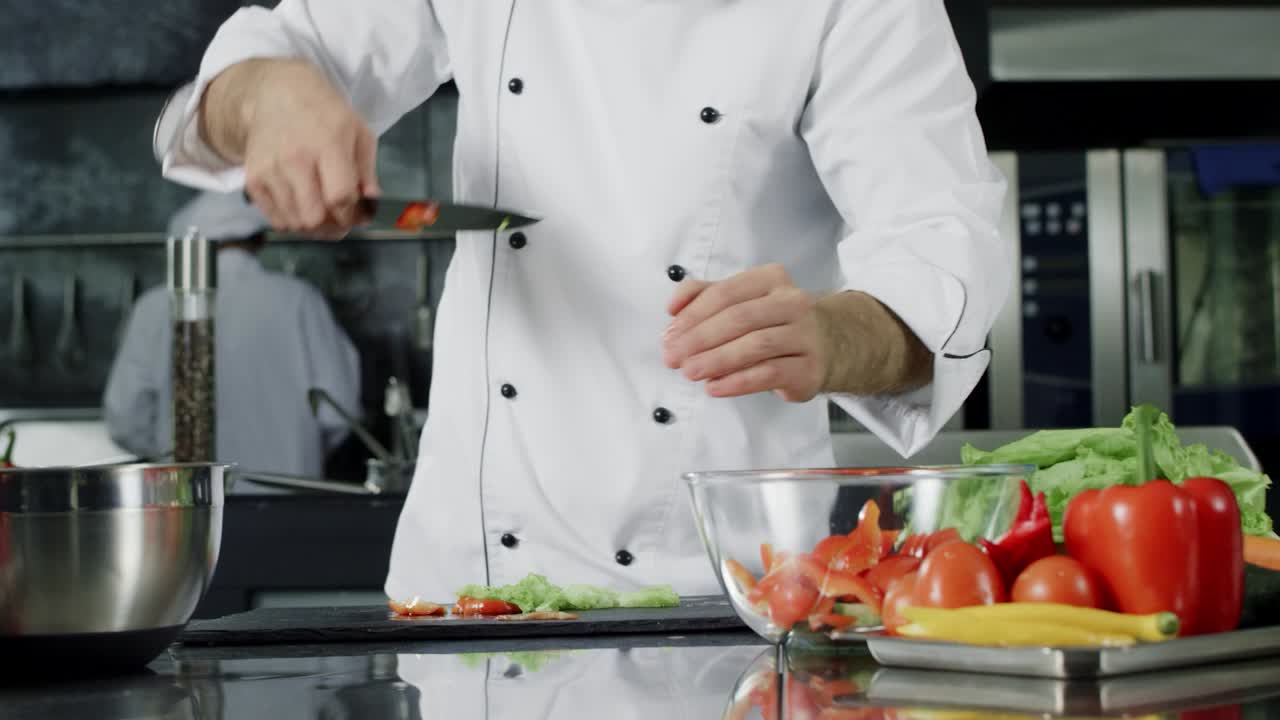 chef cocinando ensalada en la cocina. las manos del chef poniendo verduras frescas en un tazón de vidrio
