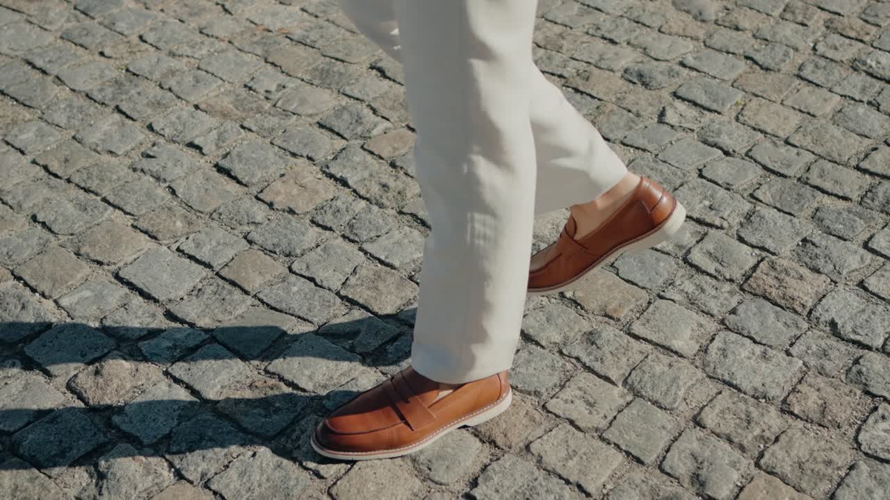 Stylish man in beige pants and brown leather shoes walking on a cobblestone street