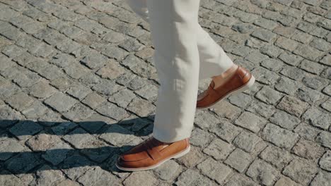 stylish man in beige pants and brown leather shoes walking on a cobblestone street