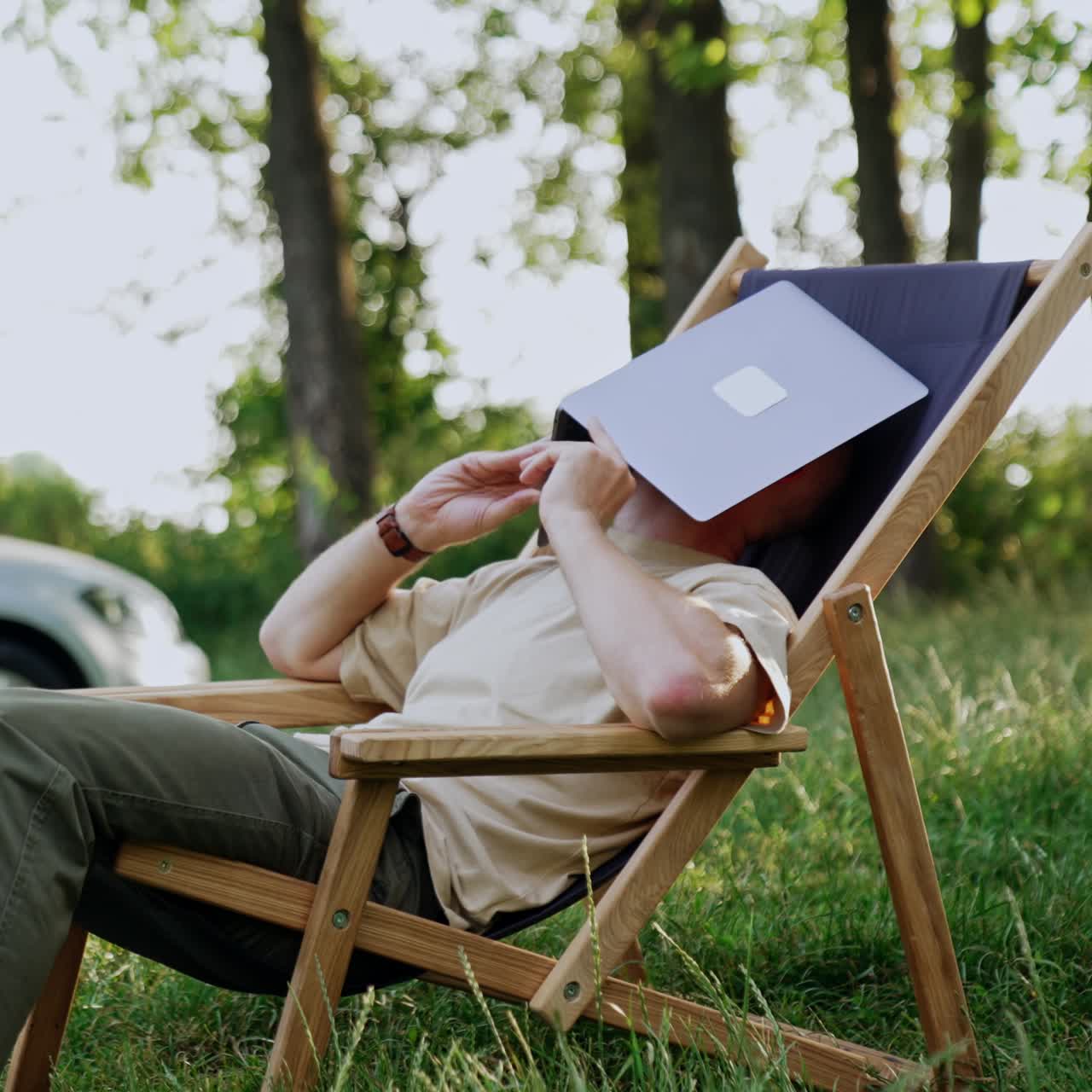 Caucasian man working remote in nature is feeling tired. Man takes a break covering his face with laptop