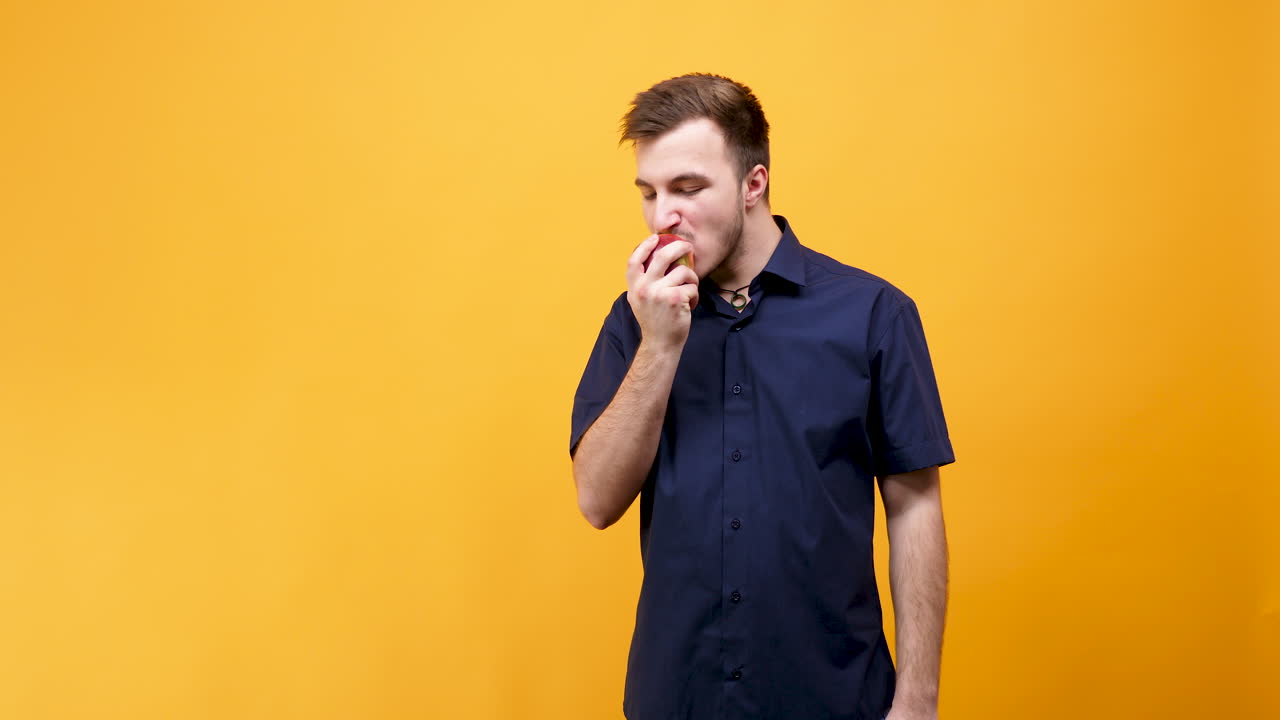 Uomo che mangia una mela su uno sfondo giallo
