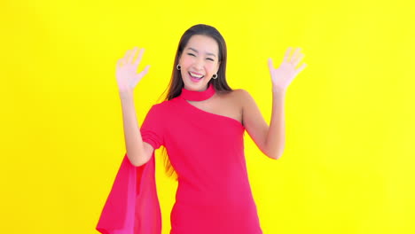 young asian woman greets in elegant fuchsia dress with yellow screen in background