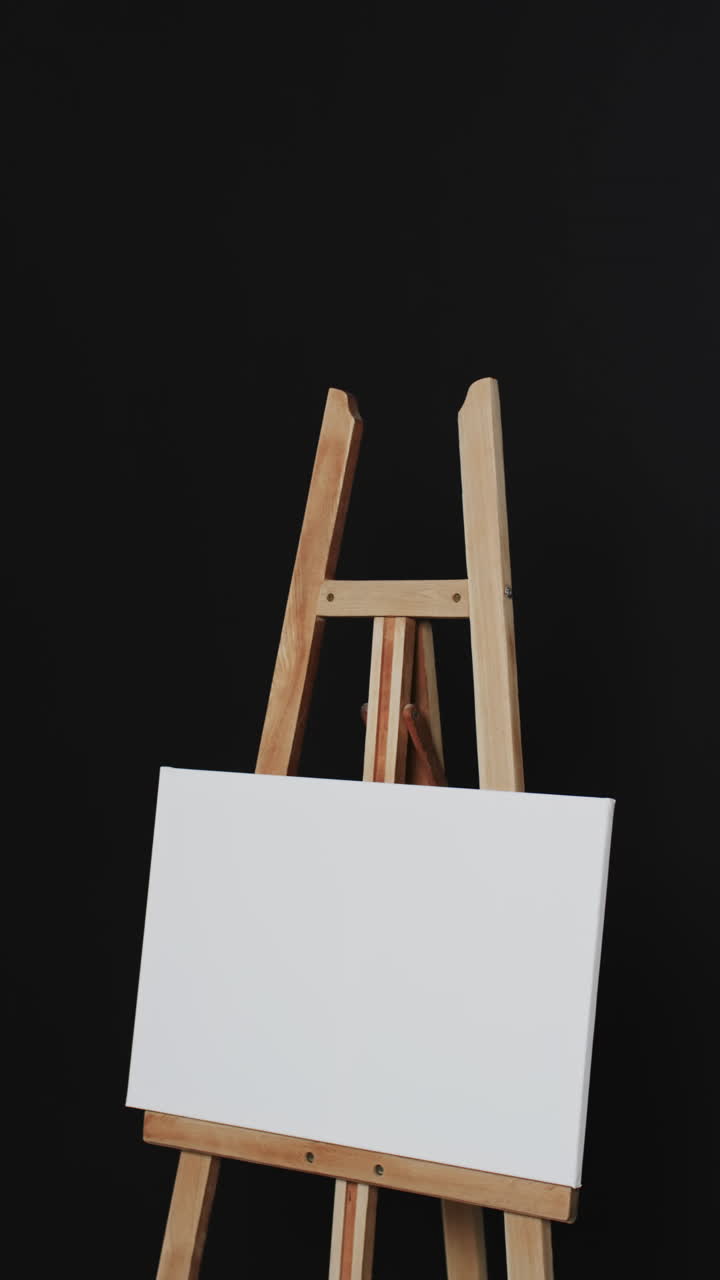 Vertical video of white canvas sign on wooden easel with copy space on black background
