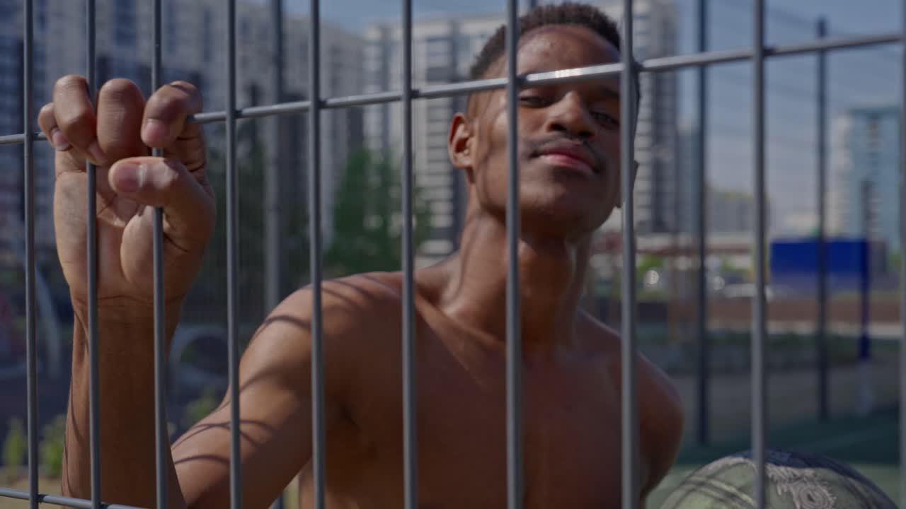 Jovem Homem Negro Segurando Bola de Basquete Atrás de Cerca em Quadra Urbana