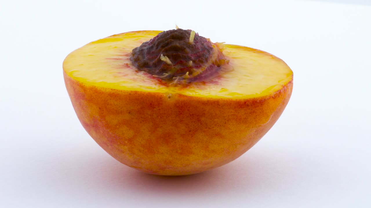 One half of peach fruits with a pit. Rotating on the turntable. Isolated on the white background. Close up. Macro.