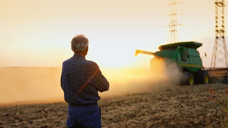 harvest at sunset in golden fields. a farmer observes a combine harvester working in golden fields during sunset, creating a picturesque rural atmosphere