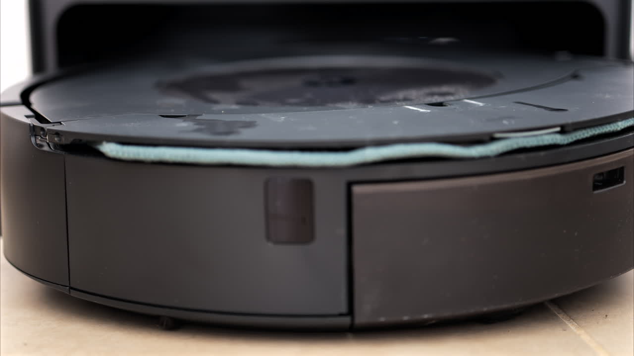 Close up of a black robot vacuum cleaner moving and rotating on the floor tiles