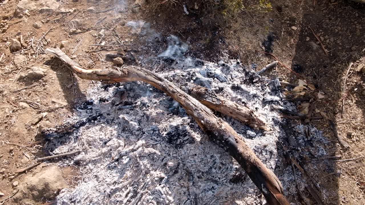 광야에서 야외에서 죽어가는 작은 모닥불에서 숯불이 피고 연기가 나는 뜨거운 불에 탄 통나무와 막대기