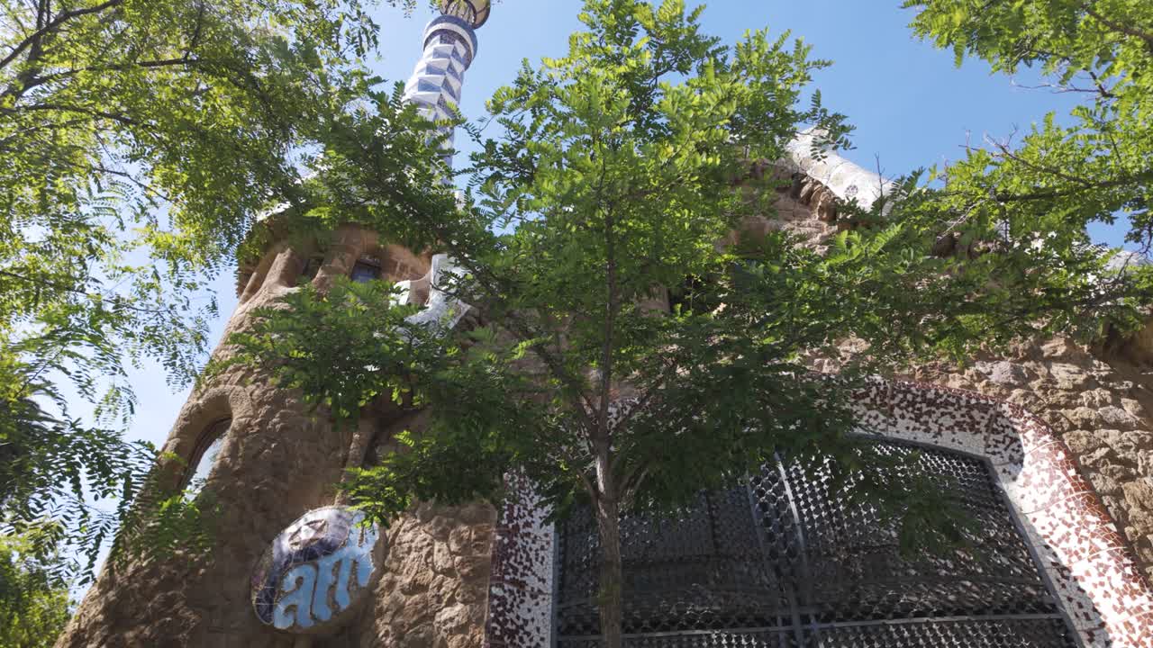 Lush green trees frame a whimsical building in park guell, barcelona, showcasing antoni gaudi's unique architectural style