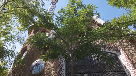 lush green trees frame a whimsical building in park guell, barcelona, showcasing antoni gaudi's unique architectural style