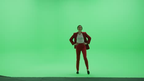green screen chroma key studio: beautiful business woman wearing stylish red suit does catwalk walk across room right to left. side view camera shot