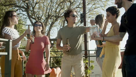 amigos felices bebiendo cerveza y comiendo nachos mientras bailan en la fiesta de la azotea en un día de verano