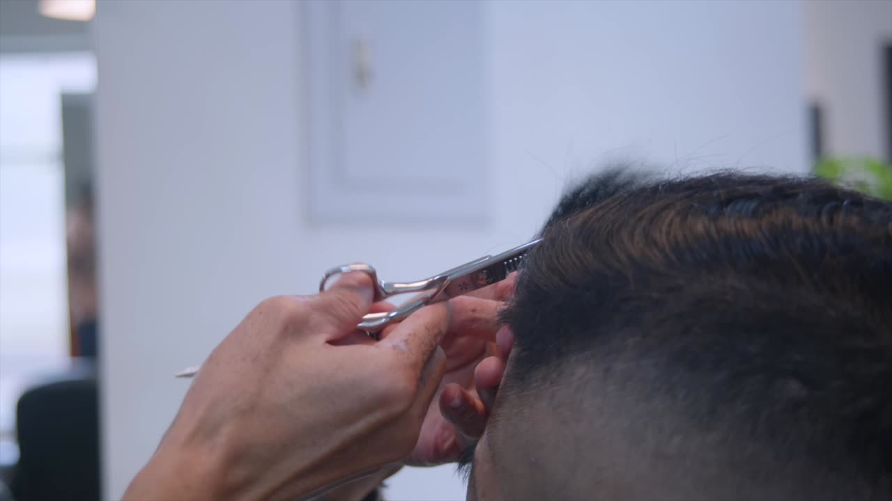 más de tijeras de peine que se utilizan en el lado delantero de la cabeza para cortar el cabello, filmado desde el lado izquierdo de las tijeras en estilo de primer plano