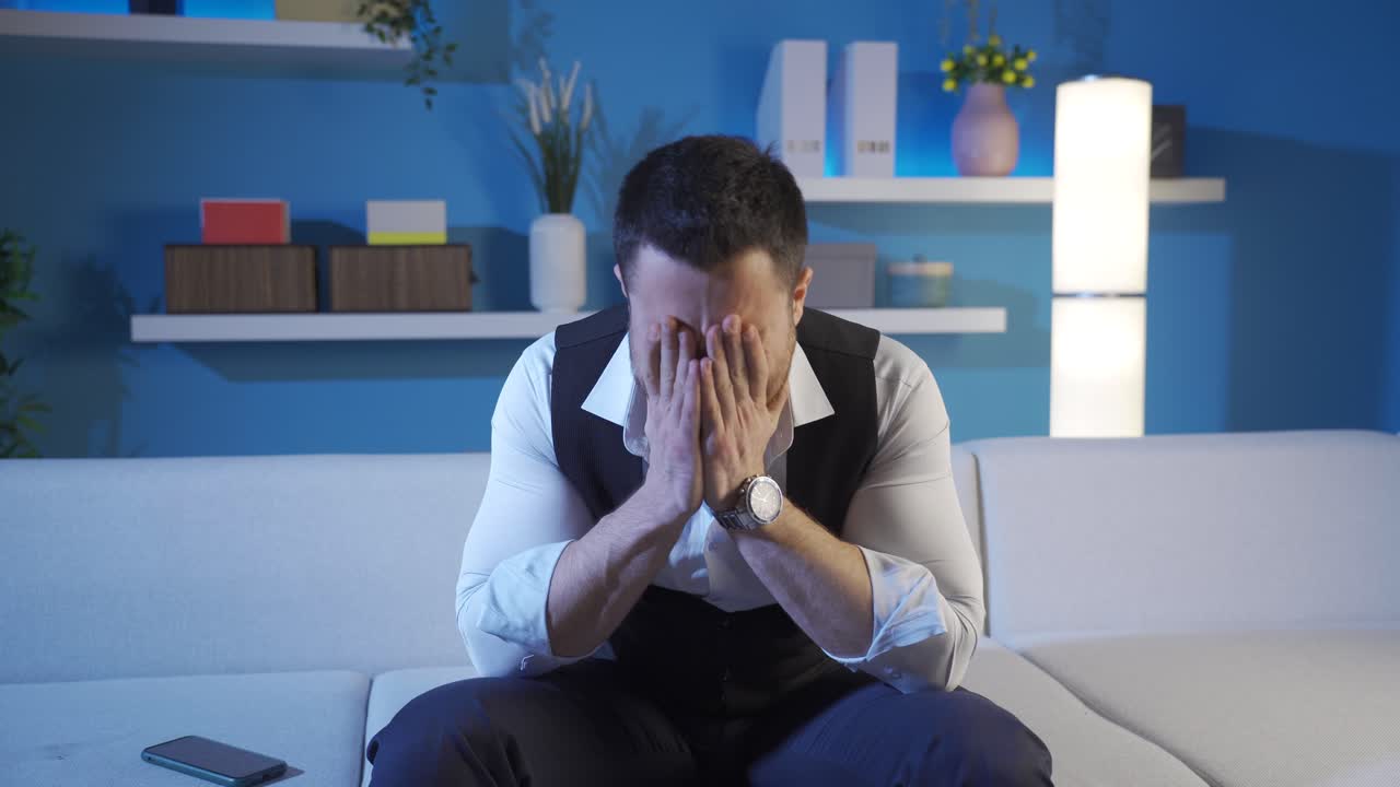 집에 앉아 있는 남자는 전화에서 본 것에 좌절하고 울면서 주위를 둘러보습니다.