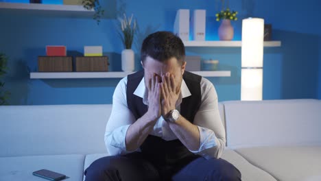 el hombre sentado en casa está frustrado por lo que vio en el teléfono y mira a su alrededor llorando.