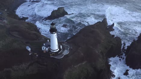 Aerial-tilt-up-descending-over-Yaquina-Head-lighthouse-and-stormy-sea,-Newport