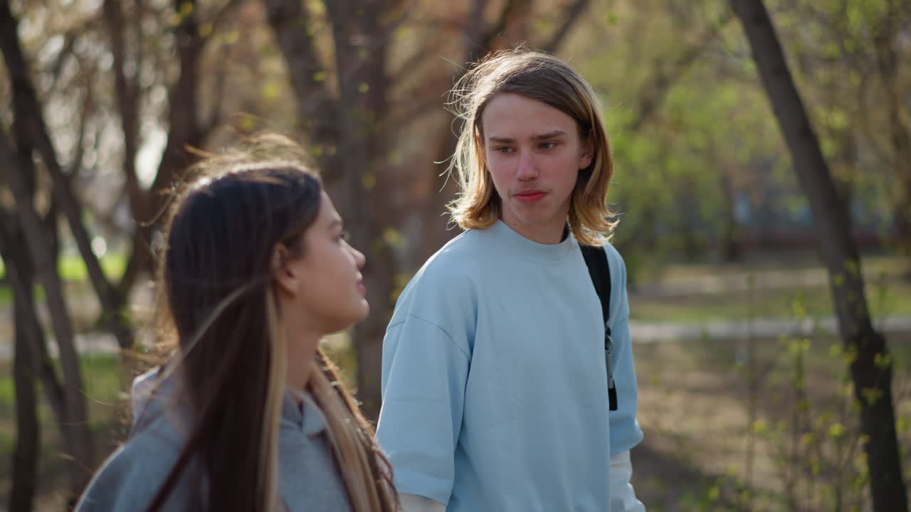 두 친구가 어색한 눈빛을 주고받으며 공원을 걷고 있어요. 어깨에는 백팩을 메고 있고, 가을 햇살이 나무 사이로 비쳐 들면서 학생들이 이야기하고, 듣고, 솔직한 순간 속에서 서로 연결되고 있네요.