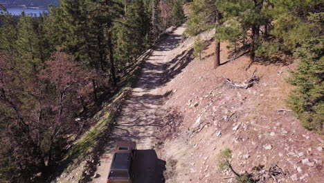 un vehículo suv oscuro conduce lentamente por un camino de fuego de montaña de tierra a través de un bosque de pinos
