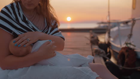 mother nursing and caressing baby sitting on the pier at sunset