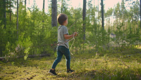 niño en el bosque recogiendo leña recogiendo leña seca en el bosque de verano en el campamento leña para el fuego del campamento en la caminata de verano